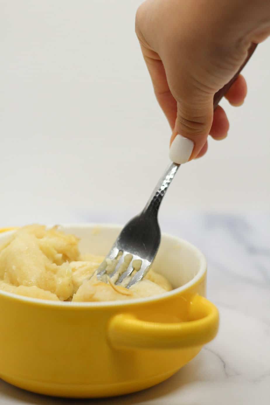 mashing bananas in yellow bowl with a fork