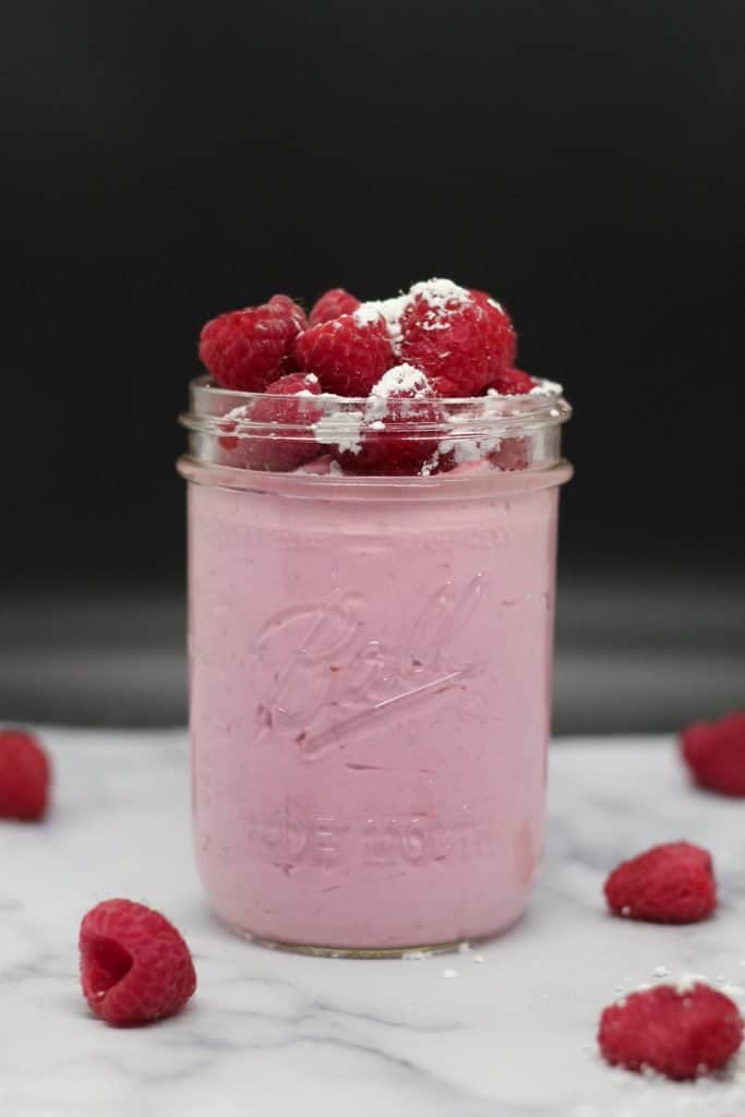 mason jar filled with raspberry mascarpone cream topped with fresh raspberries and powdered sugar on a white surface with black background