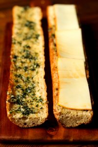 cheesy garlic bread on multigrain baguette sliced in half on brown surface