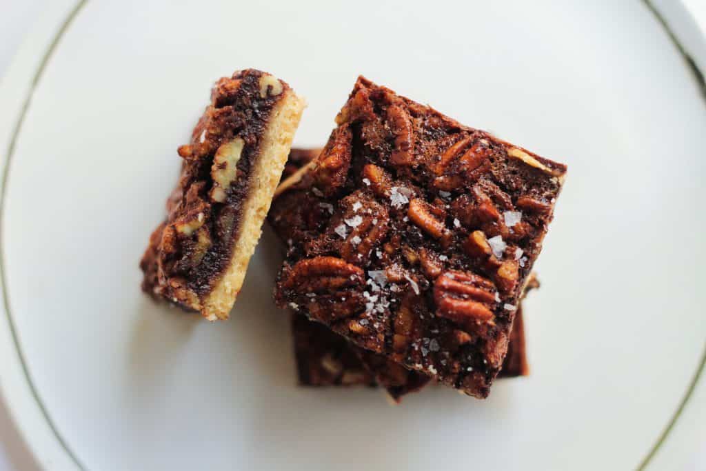Stack of pecan shortbread bars with flaky salt on top, on a white plate.