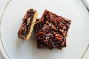 Stack of pecan shortbread bars with flaky salt on top, on a white plate.