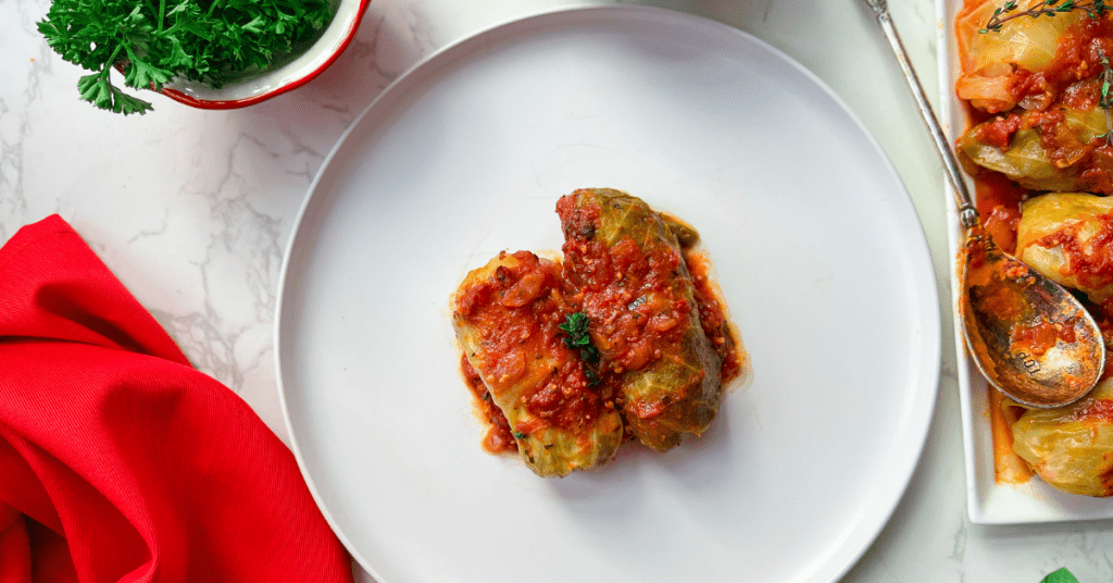 Two stuffed cabbage rolls on a white plate with a red napkin and green fresh parsley on the side.
