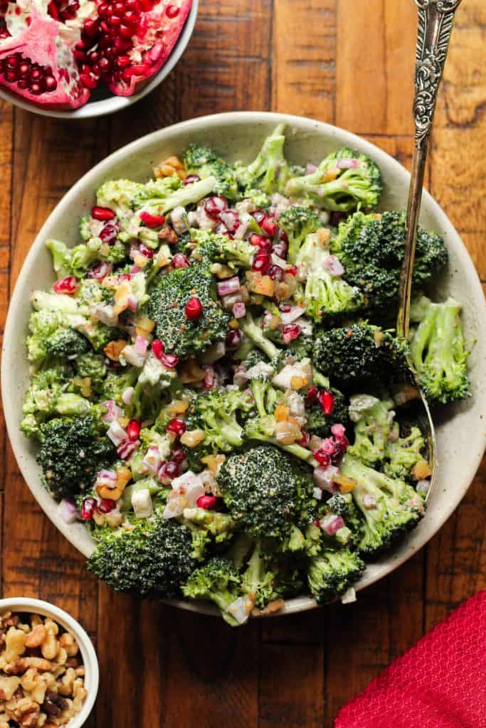 Broccoli pomegranate salad in a white bowl on a brown wooden table.