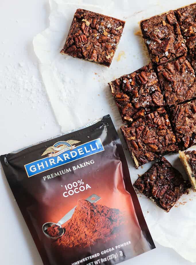 Pecan shortbread bars cut into squares - also pictured is a bag of Ghirardelli 100% cocoa powder.