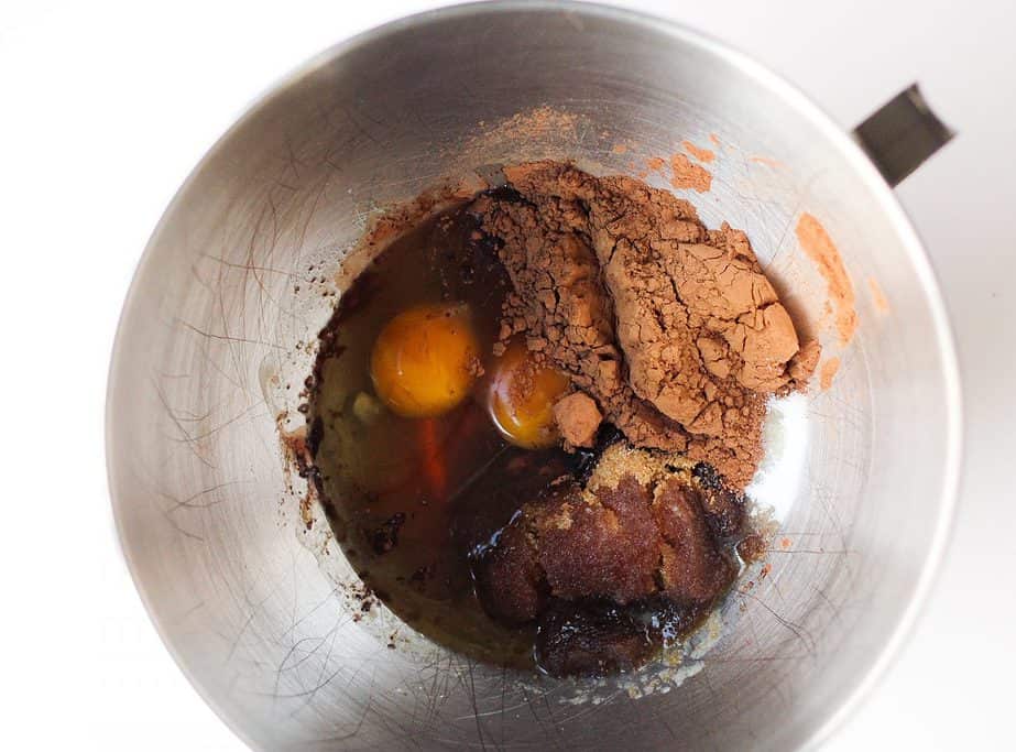 Pecan Shortbread Bars ingredients (eggs, cocoa powder, brown sugar, maple syrup) in a silver kitchenaid bowl on a white surface