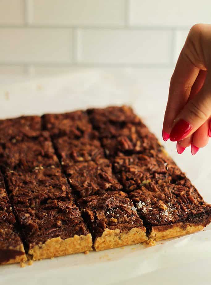 Chocolate maple pecan shortbread bars being sprinkled with flaky salt.