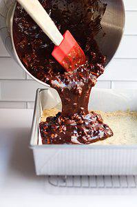 Chocolate maple pecan shortbread bars being poured over the crust in a cake pan.