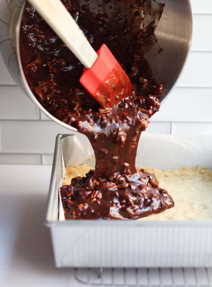 Chocolate maple pecan shortbread bars being poured over the crust in a cake pan.