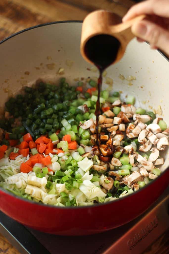 Soy sauce being added to the pot of chicken manchow soup.