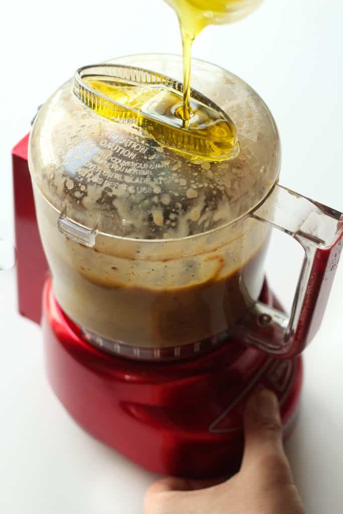 Olive oil being streamed into the mustard vinaigrette ingredients in a food processor.