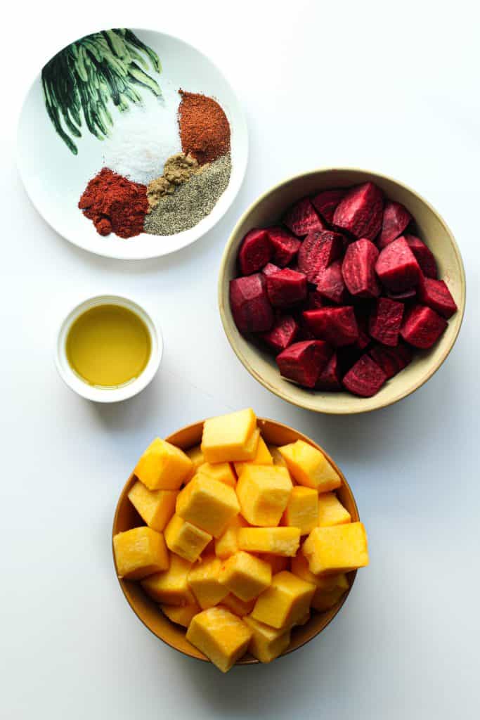 Diced beetroot and pumpkin in two separate bowls along with a plate of spices and a cup of olive oil.