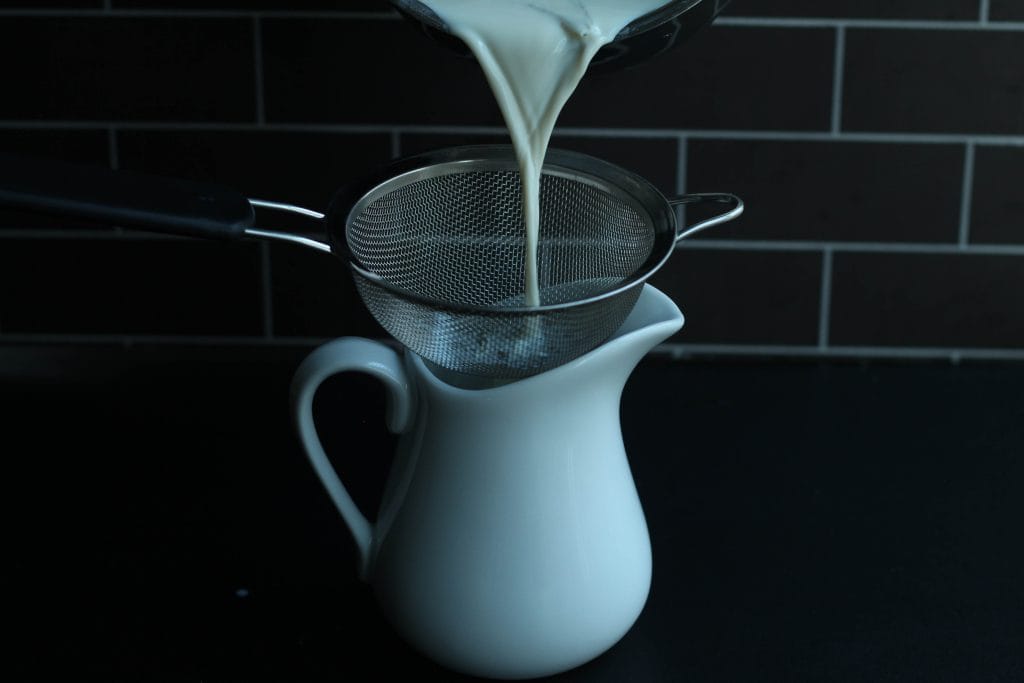Steeped milk being strained through a fine mesh strainer.