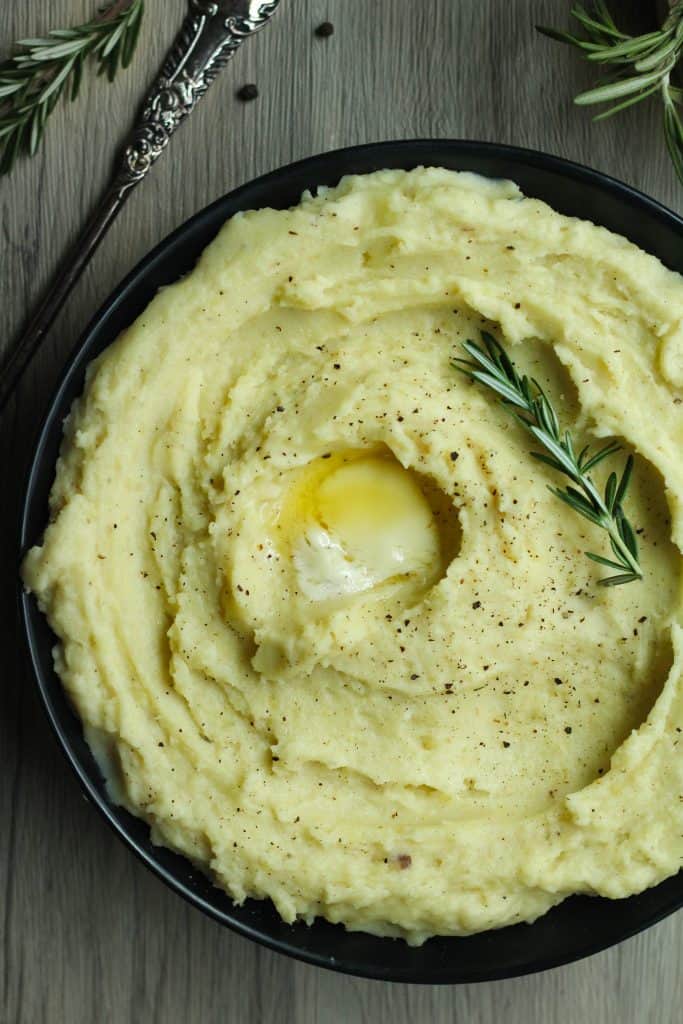 Rosemary garlic mashed potatoes with a slab of butter in the center and a spring of rosemary.