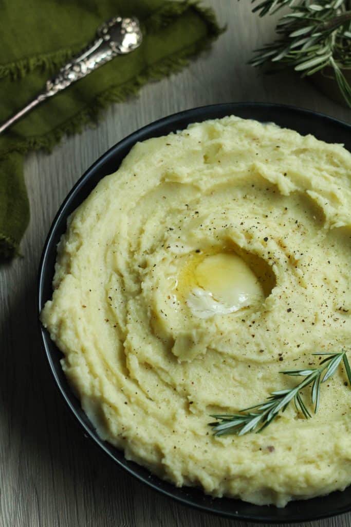 Rosemary garlic mashed potatoes with a slab of butter in the center and a spring of rosemary.