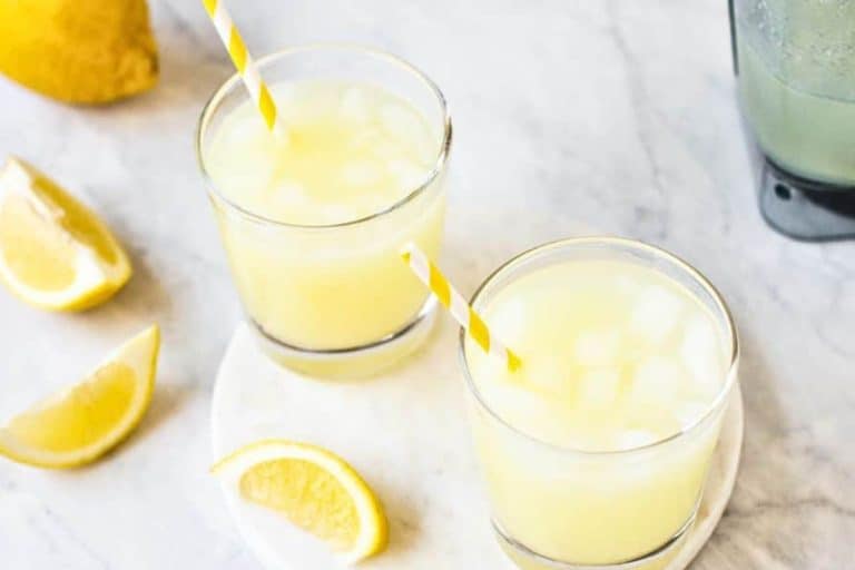 Blender whole lemon lemonade recipe with lemon wedges and yellow and white straws vegan drinks.