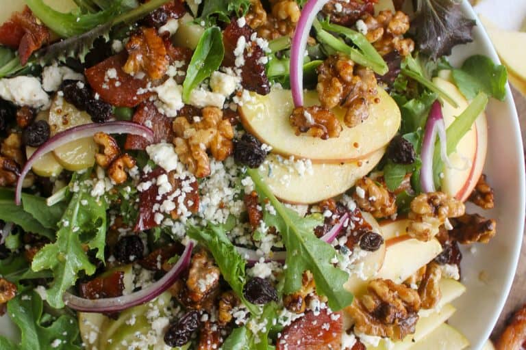 Blue cheese apple walnut salad topped with thinly sliced onions and pecans in a white bowl.