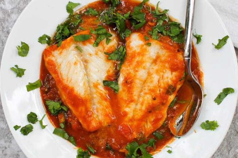 Cod curry with pumpkin garnished with fresh herbs on a white plate with a silver spoon.