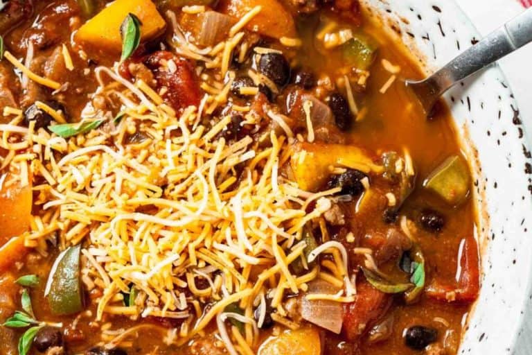 Healthy pumpkin chili recipe topped with shredded cheese in a white bowl with black specks - fall dishes for dinner