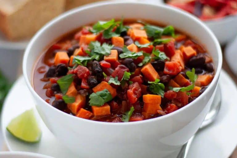 Sweet potato black bean chili garnished with cilantro and a lime wedge in a white bowl.