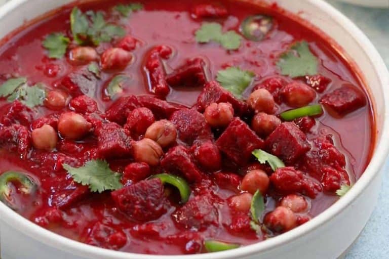 Purple colored beet curry with chickpeas in a white bowl garnished with cilantro.