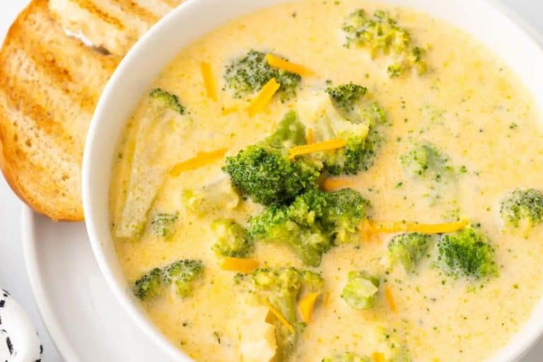 Fall soup ideas: broccoli cheddar in a white bowl on a white plate with a piece of grilled bread on the side.