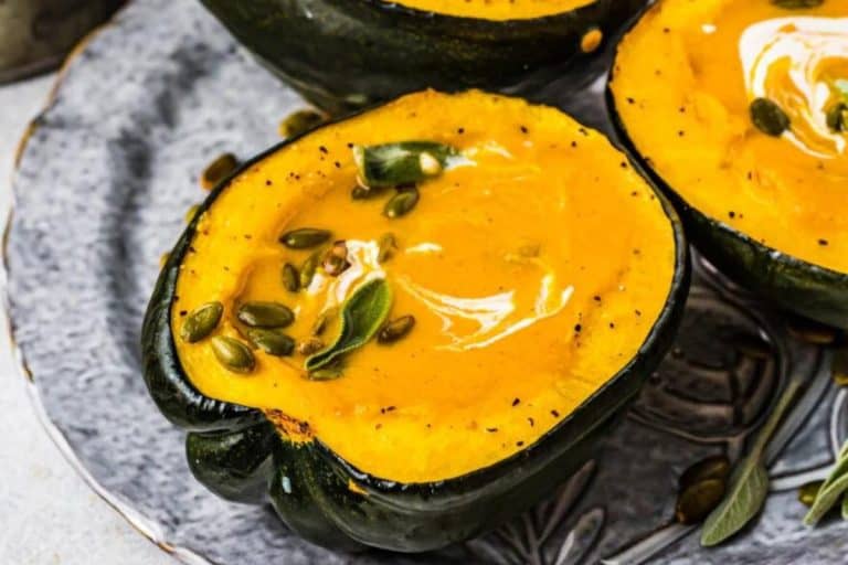 Butternut squash and sweet potato soup in a halved acorn squash with sage leaves and pepitas with cream swirled on top.
