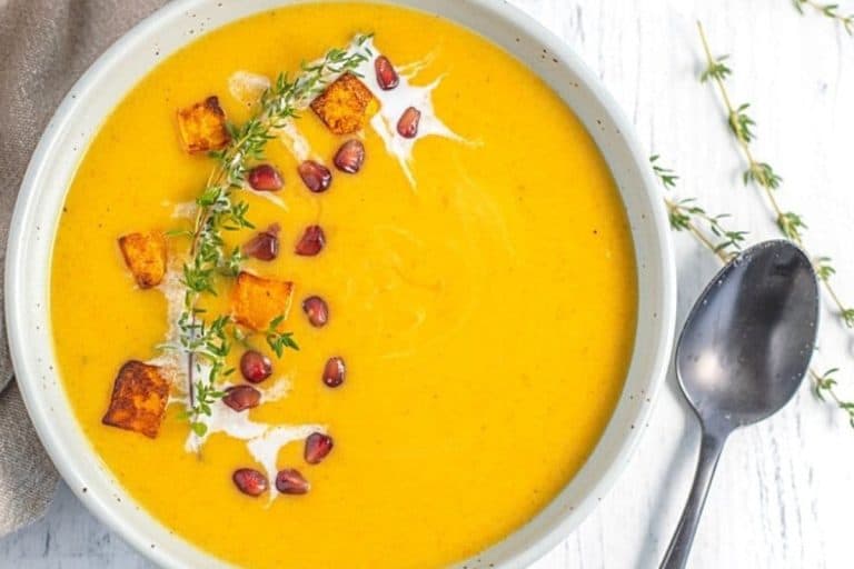 Butternut squash pear soup topped with a sprig of rosemary and pomegranate seeds with a swirl of cream.
