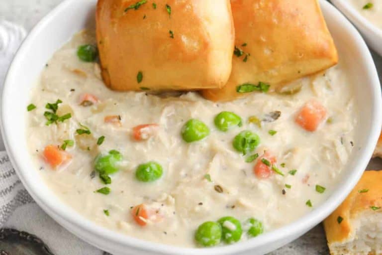 Fall soup ideas: crock pot chicken pot pie soup with peas and carrots in a white bowl with bread on the side.