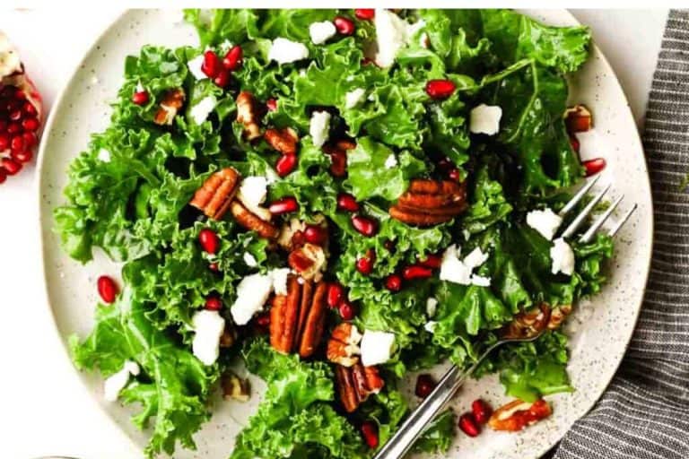 Kale pomegranate salad topped with pecans on a beige speckled plate with a gray and white striped napkin.