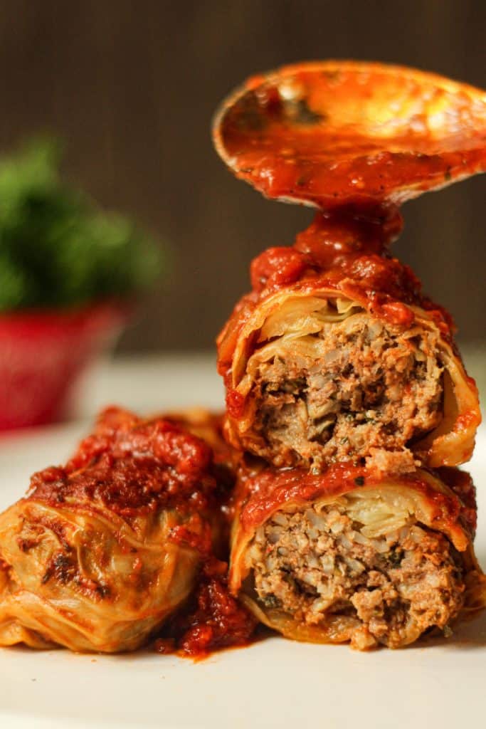 Stuffed cabbage rolls recipe cut in half being topped with a spoonful of extra sauce.