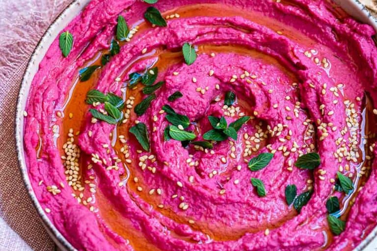 Pink swirled beetroot hummus topped with sesame seeds, mint leaves, and drizzled with oil.