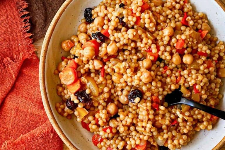 A brown and white speckled bowl filled with vegetable couscous with dried cranberries and carrots and an orange napkin.