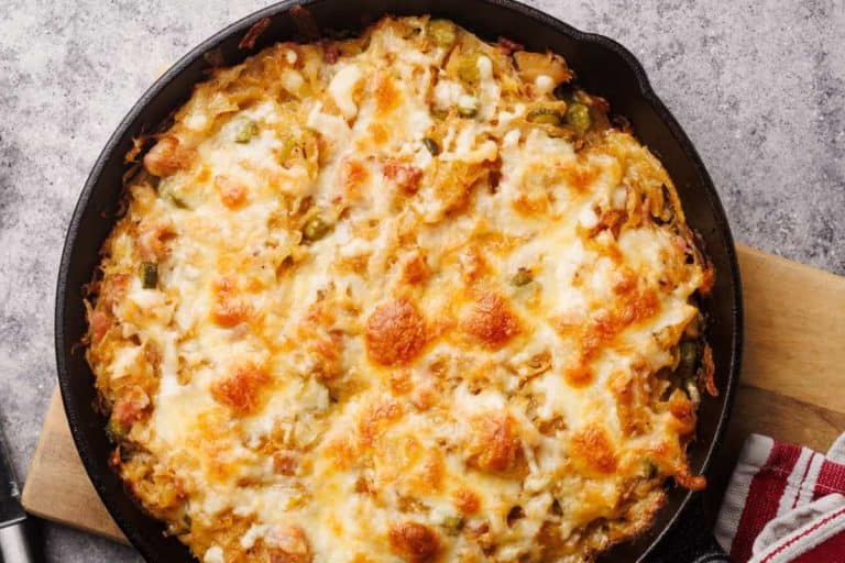 Sauerkraut casserole with a golden-brown cheesy top in a black cast iron on a brown cutting board fall potluck dishes.