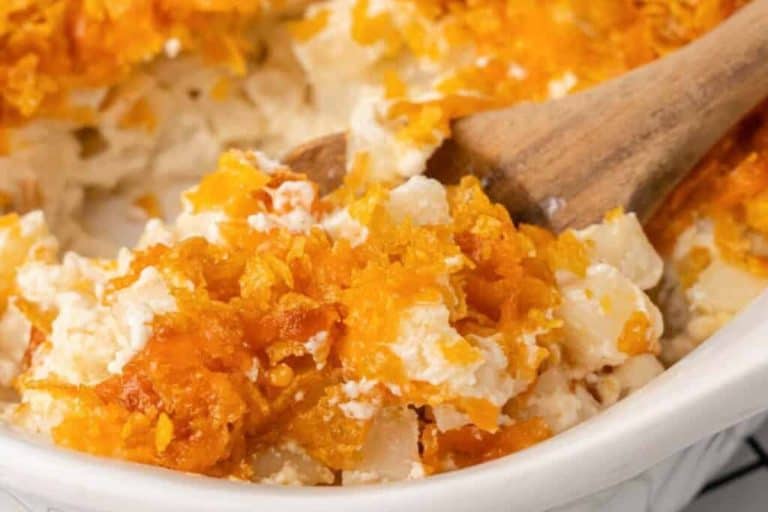 Cheesy funeral potatoes with a crispy top in a white baking dish with a wooden spoon.