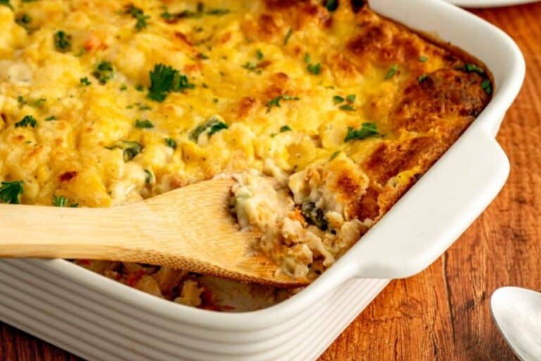 Fall potluck dishes easy chicken cobbler with a wooden spoon in a white baking dish on a wooden surface.