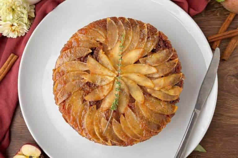 Apple upside down cake on a white plate with a silver knife and a red napkin.