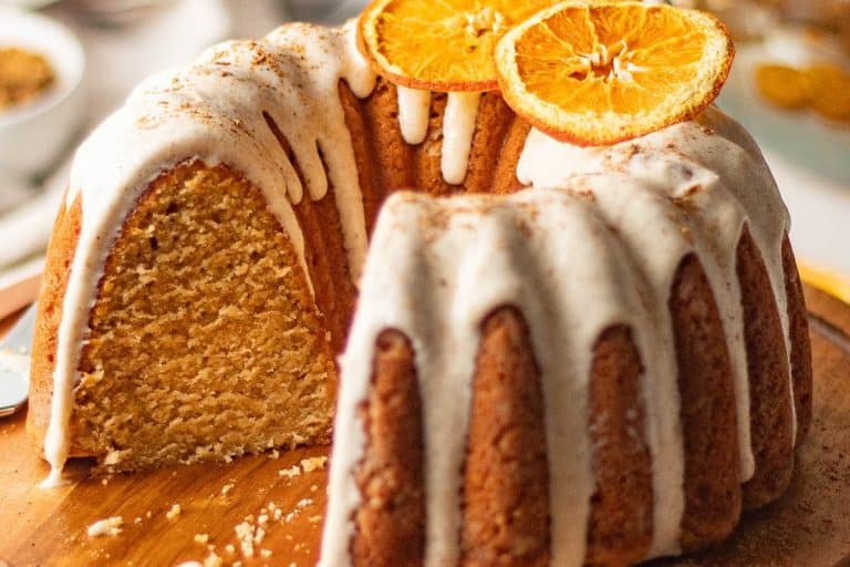 Chai sliced bundt cake with a slice missing and drizzled with icing and topped with two dried orange slices - fall dessert recipes.