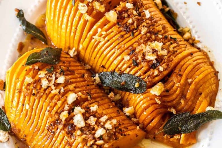 Hassleback butternut squash topped with sage leaves and breadcrumbs in a white dish fall potluck dishes.