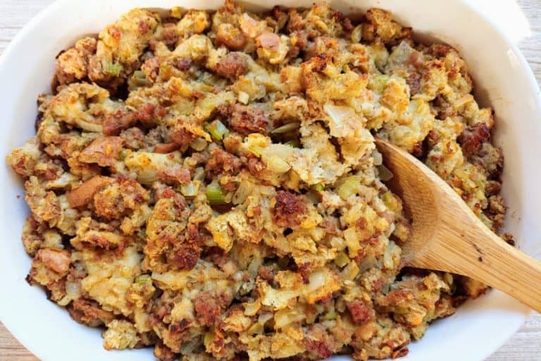 Sausage stuffing in a white baking dish with a wooden spoon fall potluck dishes.