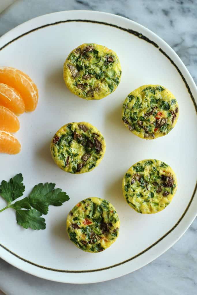 5 Veggie Egg Bites displayed on a round white plate with orange slices and a piece of parsley.