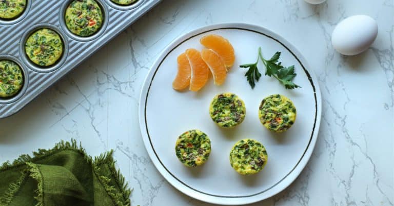 Cooked veggie egg bites on a white plate with orange slices and more egg bites in the mini muffin pan.