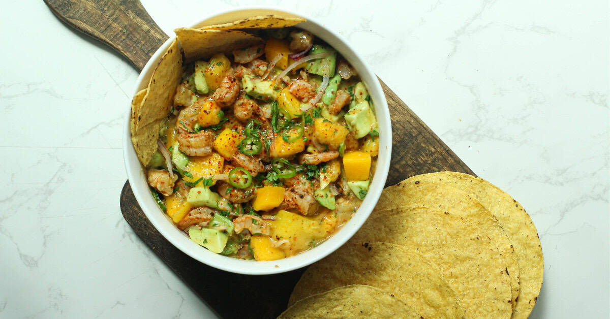 Shrimp avocado and mango salad in a white bowl on a board with tostadas.
