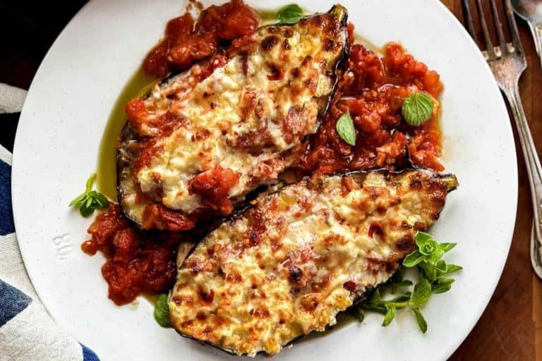 Summer dinner ideas: Greek Papoutsakia stuffed eggplant with tomato sauce and garnished with sprigs of fresh herbs.