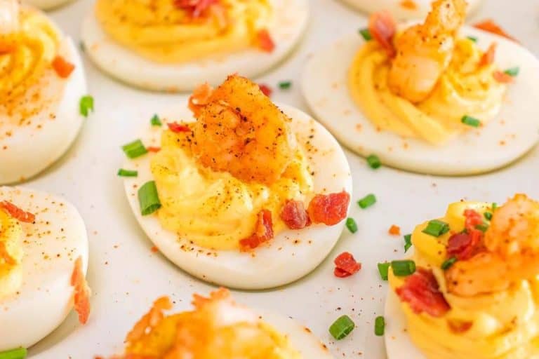 Cajun shrimp deviled eggs sprinkled with bacon bits and sliced chives on a white dish.