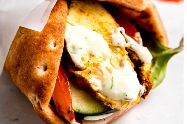 Chicken shawarma with peppers and cucumbers wrapped in a golden pita drizzled with white sauce.