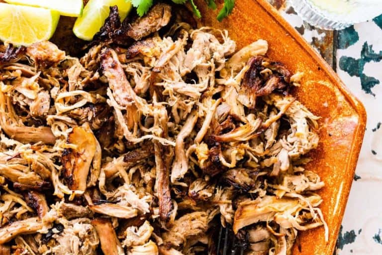 Summer dinner ideas: shredded chipotle carnitas on a burnt orange colored platter with lime wedges.