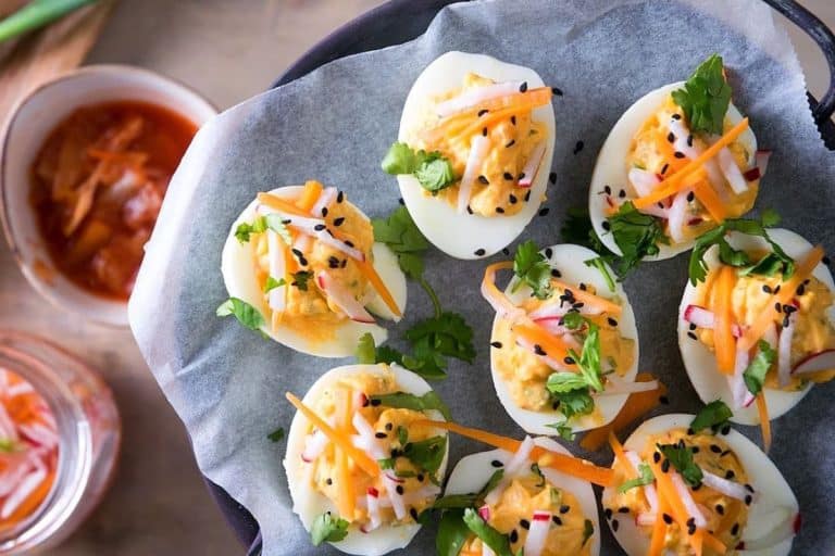 Kimchi deviled eggs topped with shredded carrots, radish, and fresh cilantro sprinkled.