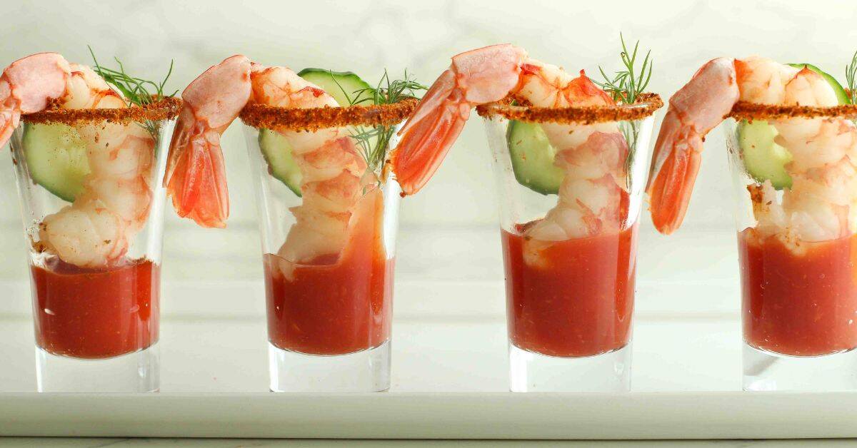 Two shrimp cocktail shooters in shot glasses with cucumber and dill sprigs.