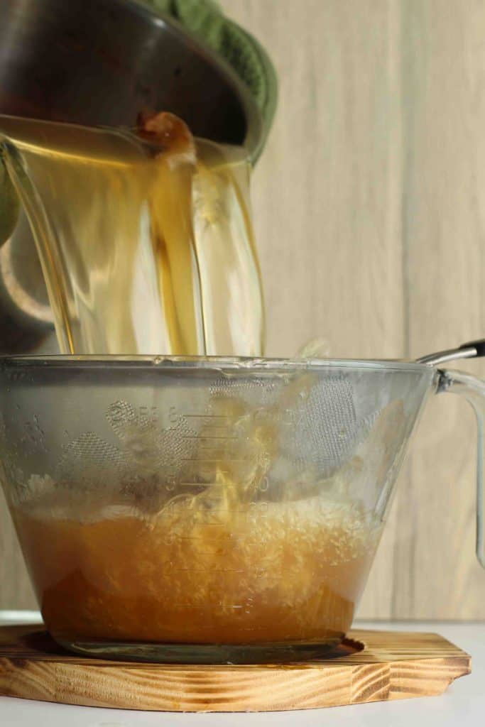A pot of homemade bone broth being poured and strained into a strainer over a bowl.