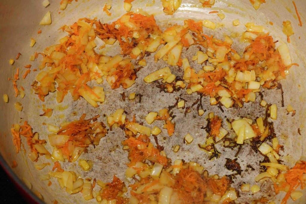 Carrots, onions, and garlic being sauteed in a dutch oven.